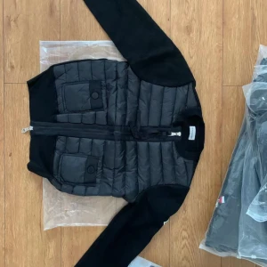  Moncler cardigan  - Snälla skriv innan ni köper!! Vid snabb köp kan ni köpa den för 2000kr. Snygg svart pufferjacka från Moncler med quiltad front, två stora fickor med knappar och dragkedja. Ärmarna är stickade för en skön kontrast och jackan har en clean look med diskret Moncler-logga på bröstet. Perfekt för dig som gillar stilren och sportig vibe.