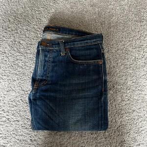 Blå nudie jeans - Säljer ett par klassiska blå slim/ skinny jeans från Nudie Jeans med snygga kontrastsömmar. Jeansen har fem fickor, normal midja och ikoniska bakfickor med Nudie-loggan. Perfekta för dig som gillar en smal passform och stilren look. Storlek 10 år