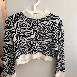 Svartvit stickad tröja från Monki - Cool stickad tröja från Monki i svartvitt vågigt mönster. Tröjan är croppad med ribbad halsringning, ärmslut och nederkant. Perfekt för dig som vill sticka ut med en unik look. Långärmad och i mjukt material som känns skönt mot huden.