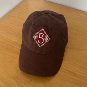 Brun keps Odell Brewing 5 Barrel - Snygg brun keps från Odell Brewing med broderad '5' framtill och texten '5 Barrel Pale Ale' baktill. Kepsen är i 100% bomull och har justerbar rem bak. Märke: Ouray Sportswear. Perfekt för dig som gillar unika bryggerikepsar.