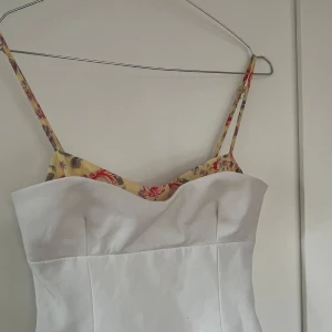 Blus från Zara - Supersöt vit blus från Zara med smala axelband och blommigt mönster i gult, rött och lila upptill. Storlek xs och använd ca 2 gånger 