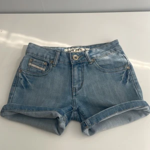 Ljusblå jeansshorts Long Chang - Snygga ljusblå jeansshorts från Long Chang med klassisk femficksdesign och dekorativa broderier med pärlor på bakfickorna. Shortsen har normal passform, midwaist och är tillverkade i mjukt denim. Perfekta för varma dagar