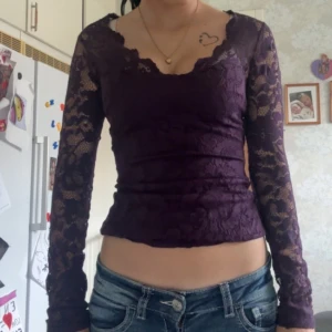 Lila spetsblus med lång ärm - Säljer en lila, figurnära blus i spets med långa ärmar och v-ringad hals. Blusen är genombruten med snyggt spetsmönster och har en croppad passform. Perfekt för dig som vill ha en feminin och trendig look.