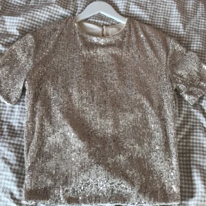 Glittrig paljettopp från H&M XS - Supersnygg glittrig topp från H&M i champagnefärg, täckt med paljetter. Kortärmad modell med rund hals och liten öppning med knapp i nacken. Perfekt för att sticka ut och ge extra bling till din outfit. Perfekt fest-topp! Öppen för prisförslag 
