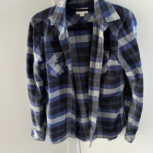 Flanell skjorta - Säljer en snygg rutig skjorta från Diesel i blått, svart och vitt. Skjortan har klassisk krage, knappar framtill och två bröstfickor med lock. Perfekt för dig som gillar en avslappnad men cool stil.