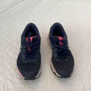 Blå Asics sneakers strl 35.5 - Snygga Asics GT-2000 sneakers i mörkblått med rosa och vita detaljer. Ovandel i mesh och syntet, med klassisk Asics-logga på sidan. Skorna har snörning och en bekväm, stötdämpande sula – perfekta för träning eller långa promenader. Dock väldigt smutsiga men går nog bort i tvätten.