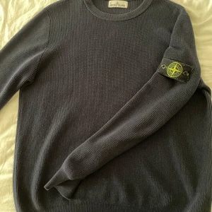 Mörkblå stickad Stone Island tröja - Säljer en mörkblå stickad tröja från Stone Island i storlek M. Tröjan har ribbad struktur, rund hals och den klassiska Stone Island patchen på vänster ärm. Perfekt tröja till hösten.
