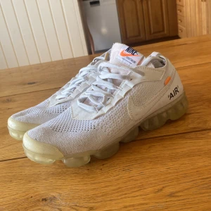 Off-White x Nike Air Vapormax Vit storlek 43 - Säljer ett par Off-White x Nike Air Vapormax i vit med transparent sula och klassiska Off-White detaljer. Skorna har stickad ovandel, snörning och tydlig 'AIR'-text på sidan. Perfekt för dig som gillar unika och hypade sneakers.