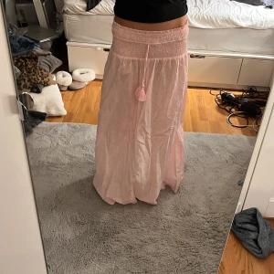 Ljusrosa långkjol med snörning - Supersöt ljusrosa långkjol med snörning i midjan. den har små vita detaljer.