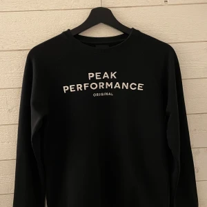Svart Peak Performance sweatshirt - Svart sweatshirt från Peak Performance med vit broderad logga på bröstet. Klassisk rund hals och långa ärmar. Mjuk bomullskänsla och normal passform. Använd två gånger och i gott skick. Hör av er vid funderingar 🙂