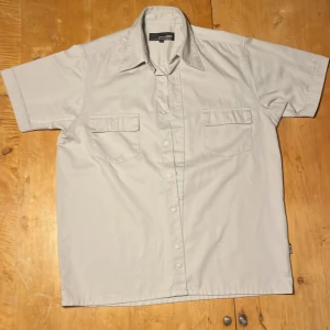 Ljusgrå kortärmad skjorta Jack & Jones - Kortärmad skjorta från Jack & Jones i ljusgrå färg. Klassisk krage, två bröstfickor med lock och knäppning framtill. Skjortan är tillverkad i mjuk bomull och har en clean, stilren look som passar perfekt till jeans eller shorts.