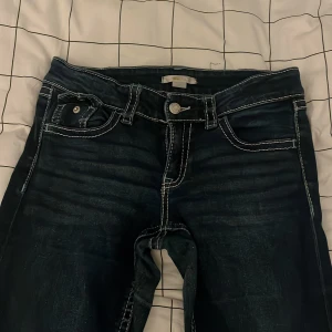 Mörkblå jeans från Gina Tricot - Snygga mörkblå jeans från Gina Tricot med kontrasterande vita sömmar och coola fickdetaljer bak med lock och knapp. Klassisk femficksmodell och knappstängning framtill. Perfekta för dig som gillar en trendig och avslappnad look.
