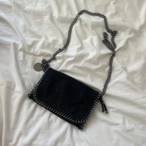 Svart axelväska  - Svart axelväska i mocka. Väskan har magnetlås och ett innerfack med dragkedja. 