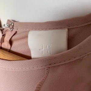 Ljusrosa långklänning med volanger H&M - Säljer en ljusrosa långklänning från H&M med volangdetaljer längs axlarna. Klänningen har ärmlös design och ett mjukt, flytande tyg som ger en elegant siluett. Perfekt för dig som gillar romantiska och feminina plagg.