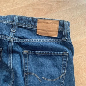Blå jeans från Jack & Jones relaxed fit - Säljer ett par klassiska blå jeans från Jack & Jones i relaxed fit. Modellen har raka ben, fem fickor och snygga kontrastsömmar. Jeansen har normal midja och är tillverkade i slitstarkt bomullsdenim. Perfekt för dig som gillar en chill och tidlös stil.