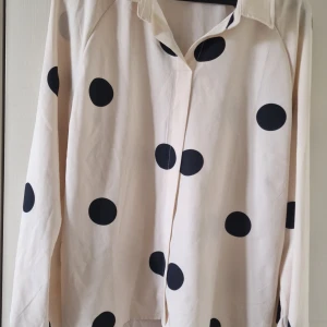 Prickig beige skjorta från SHEIN XL - Snygg beige skjorta från SHEIN i storlek XL med stora svarta prickar. Skjortan har klassisk krage, dolda knappar framtill och långa ärmar. Perfekt för dig som gillar statement-mönster och vill sticka ut lite extra.