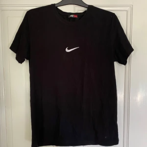 Svart Nike t-shirt  - Svart t-shirt från Nike i mjuk bomull med klassisk vit swoosh på bröstet och vänster ärmen. Enkel och clean design med rund hals och korta ärmar. Perfekt för dig som gillar sportiga och stilrena plagg. Passar perfekt till storlek M👍
