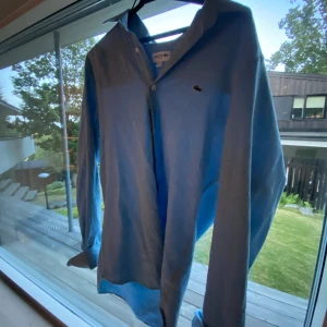 Ljusblå skjorta från Lacoste - Säljer nu en skön blå linne Lacoste skjorta perfekt inför sommaren. Söker nu för 449 men pris kan diskuteras. Inga defekter.