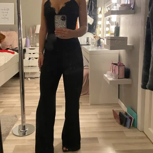 Jumpsuit - Säljer en svart jumpsuit med spets vid bysten. Jumpsuiten är ganska lång i benen och har en dragkedja bak i ryggen.