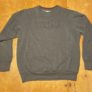 Grå sweatshirt från Roberto Jeans XL - Mörkgrå sweatshirt från Roberto Jeans i storlek XL. Tröjan har broderad text 'VINTAGE' framtill, rund halsringning och ribbade muddar vid ärmslut och nederkant. Tillverkad i mjuk bomullsblandning, perfekt för chill dagar. Det sägs att den är XL men jag har storlek M/L och den passar perfekt, bara och fråga om bilder! 