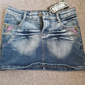  Jeanskjol från Ice Tee - Snygg kort jeanskjol från Ice Tee med slitna detaljer och broderade fickor i rosa och grönt. Köptes second hand i danmark men har inte fått någon andvändning av den.