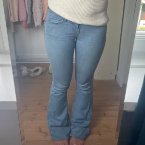 Ljusblå bootcut jeans - Säljer ett par ljusblå jeans med bootcut-modell och klassisk femficksdesign. Jeansen har låg midja och är tillverkade i mjukt denimtyg som sitter snyggt över höfterna och låren innan de släpper ut vid bensluten.