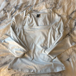 Ljusblå långärmad topp från SHEIN - Säljer en stilren väldigt ljusblå nästan vit långärmad topp från SHEIN i storlek S. Toppen har en fyrkantig ringning och är gjord i ett mjukt, glansigt material som ger en snygg look. Perfekt att matcha med jeans eller kjol för en trendig outfit.