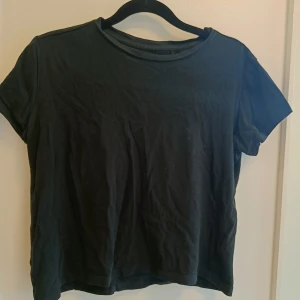 Svart croppad t-shirt - En enkel svart croppad t-shirt med rund hals och korta ärmar. Perfekt basplagg att styla med jeans eller kjol. Mjuk och skön känsla, passar till många olika looks.