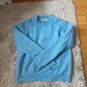 Ljusblå stickad tröja från Zara - Mysig ljusblå stickad tröja från Zara i storlek S. Tröjan har rund hals, ribbade muddar vid ärmslut och nederkant samt långärmad passform. Perfekt för dig som gillar enkel och clean stil med en pop av färg.