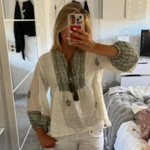 Vit blus med gröna broderier - Supersöt vit blus med gröna broderade detaljer och snörning vid halsen.  Bra skick (inte min bild,skickar fler på förfrågan) använt fåtal gånger och säljer då jag inte fått mycket användning av den