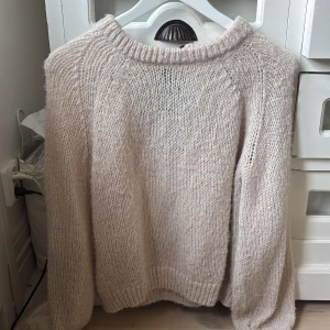 Ljusrosa stickad tröja med rosett - Supermysig beige stickad tröja från Vila i storlek S. Tröjan har långärmade ärmar, rund halsringning och en svart rosett bak i nacken som extra detalj. Perfekt för lager-på-lager och chill höst- och vinterstil.