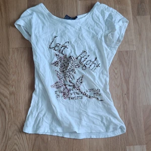 Vintage top - Säljer en vit baby-tee från Zeana Outfitters med ett coolt leopardmönster och röda detaljer. T-shirten är kortärmad och tillverkad i bomull och spandex för en skön passform. Perfekt för dig som vill ha en unik och vintage stil