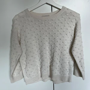 Vit stickad tröja med prickar - Säljer en söt vit stickad tröja med ett prickigt mönster. Tröjan har långa ärmar och ribbade kanter vid hals, ärmslut och nederkant. Perfekt för kyliga dagar!💕