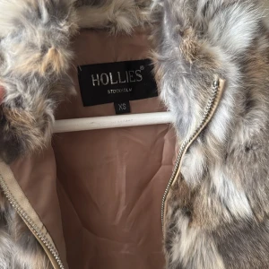 Pälsväst från Hollies - Säljer en lyxig och stilren pälsväst(kanin) från Hollies i storlek XS. Västen har en naturlig färgpalett med inslag av grått, brunt och beige. Perfekt för att hålla sig varm och trendig under kyliga dagar.