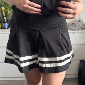 Svart kortkjol med vita ränder - svart kortkjol med vita ränder längst ner. Kjolen har en dragkedja på sidan. (Katt och kanin finns i hemmet) 