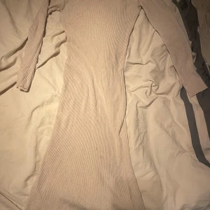 Beige ribbad långklänning - Säljer en stilren beige ribbad långklänning med långa ärmar. Perfekt för en elegant och avslappnad look. Klänningen har en smickrande passform och är gjord i ett mjukt material.