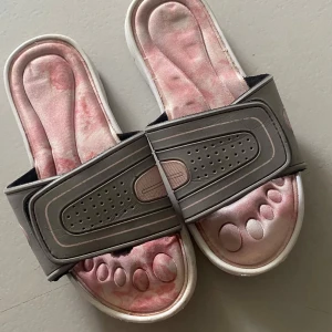 Grå ock rosa sandaler med justerbar rem - Säljer ett par bekväma sandaler i grått och rosa med justerbar rem. Sandalerna har en unik design med upphöjda mönster på fotbädden för extra komfort.