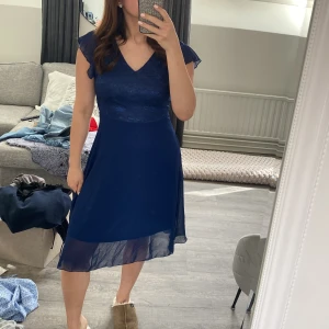 Marinblå klänning med spetsdetaljer - Säljer en elegant marinblå klänning med v-ringning och spetsdetaljer på överdelen. 