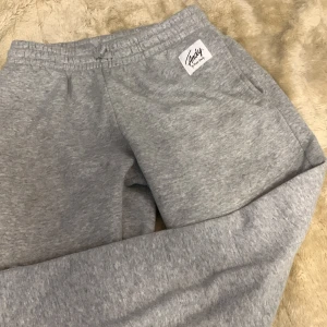 Grå mjukisbyxor från Andy by Frank Dandy - Säljer ett par grå mjukisbyxor från Andy by Frank Dandy. Byxorna har en elastisk midja och sidofickor, perfekta för en avslappnad stil. Märkeslappen sitter snyggt på sidan.