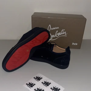 Svarta sneakers från Christian Louboutin - Snygga svarta sneakers från Christian Louboutin med den ikoniska röda sulan. Skorna har en stilren design med snörning och är tillverkade i mocka. Perfekta för att ge din outfit en lyxig touch.