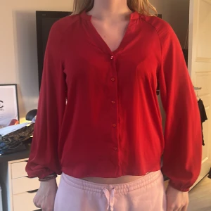 Röd blus med knappar - Snygg röd blus med knappar framtill och långa ärmar. Perfekt för en stilren look. Blusen har en lös passform och är tillverkad i ett mjukt & glansigt material. Köpte för 500kr men använt en gång
