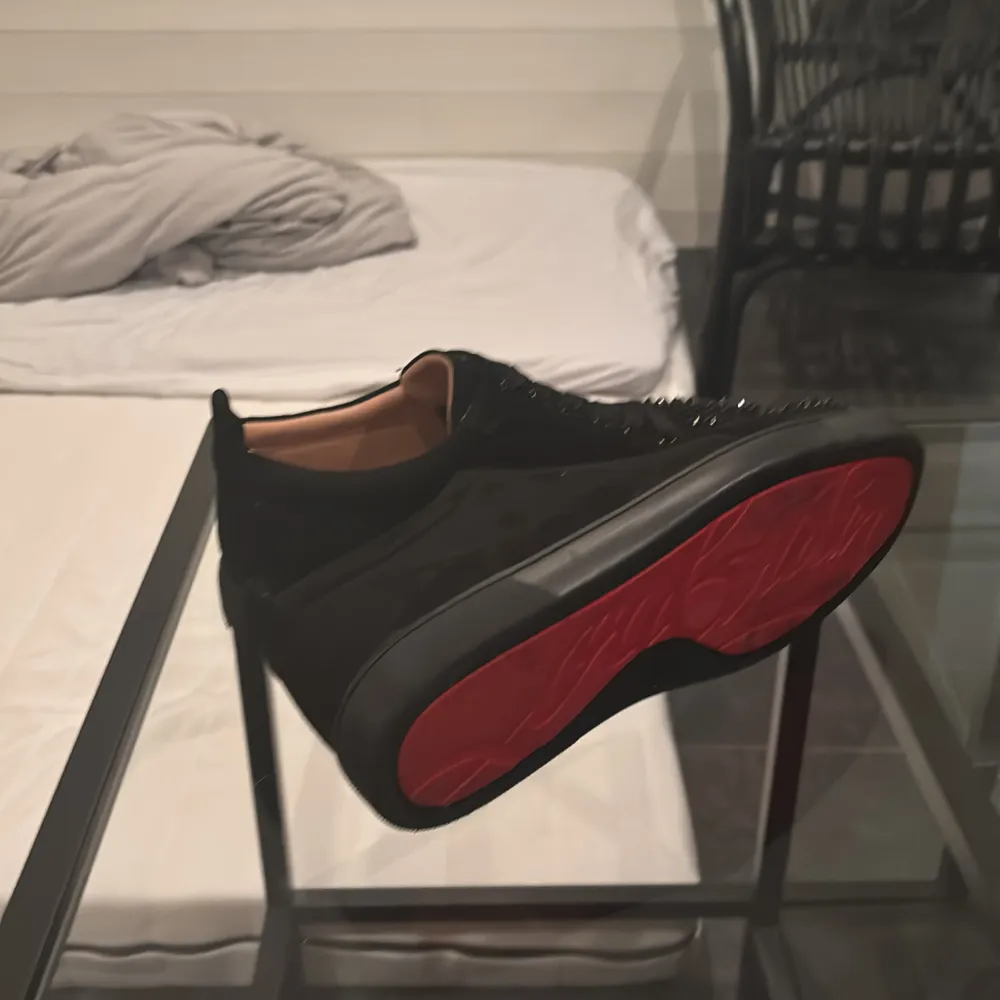 Snygga svarta sneakers från Christian Louboutin med ikoniska röda sulor och nitar på tån. Skorna har en snörning och är tillverkade i skinn, vilket ger skon en lyxig känsla. Perfekt för att ge din outfit en edgy touch. En nit fattas men de syns inte . Kengät.