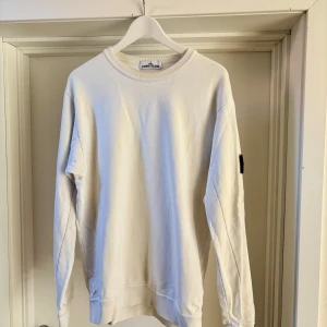 Vit sweatshirt från Stone Island - En vit tunnare sweatshirt som är i storlek L. Finns missfärgning runt halsen och ett litet litet hål i armhålan som inte gör något. 