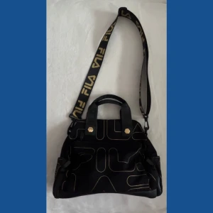 Svart axelväska från Fila - Snygg svart axelväska från Fila. Den är mellan stor väska.                                                                         Använd bara 5 gånger. 