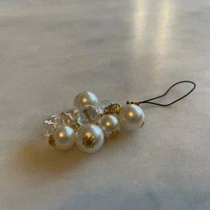 hängare med vita pärlor och klara kristaller - Elegant hängare med vita pärlor och klara kristaller, sammanlänkade med guldfärgade detaljer. Perfekt som en stilfull accessoar för att ge en touch av lyx till dina nycklar eller väska.