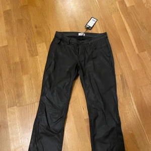 Svarta coated byxor från Weekday - Snygga svarta coated byxor från Weekday. De har en stilren design med normal passform och knappar i midjan. Perfekta för en trendig look.💕