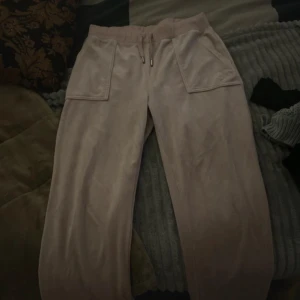 Rosa mjukisbyxor från Juicy Couture - Säljer ett par rosa mjukisbyxor från Juicy Couture. Byxorna har en bekväm passform med elastisk midja och snörning. De har praktiska fickor med knappar på baksidan för extra stil och funktionalitet. Lite mörk smutsiga på slutat av baksidan och stålen på snörena är lite rostig men annars helt okej