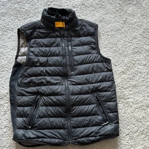 Svart dunväst från Parajumpers - Säljer en svart dunväst från Parajumpers. Västen är superlätt och har en dragkedja framtill samt två praktiska fickor med dragkedja. Perfekt för lager-på-lager under kyliga dagar.