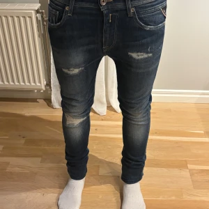 Blå Replay jeans - Snygga blå jeans från Replay med en skinny passform. De har en klassisk femficksdesign och slitna detaljer på framsidan för en trendig look. Perfekta för en stilren vardagsoutfit. Jag skulle dock säga att de sitter lite mer åt slimm på mig. 