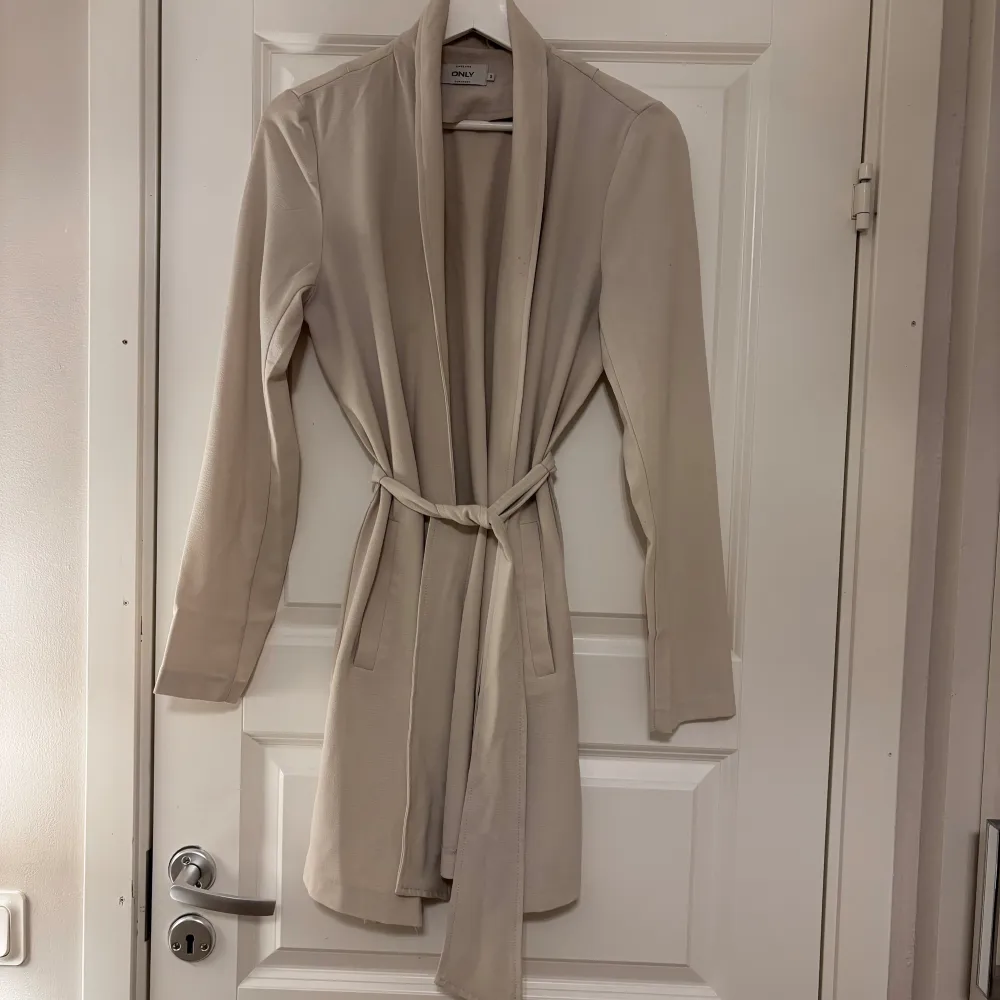 Elegant beige, tunnare kappa från Only med knytbälte i midjan. Den har en stilren design med långa ärmar. 💗Storlek XS/S. 150kr.. Takit.